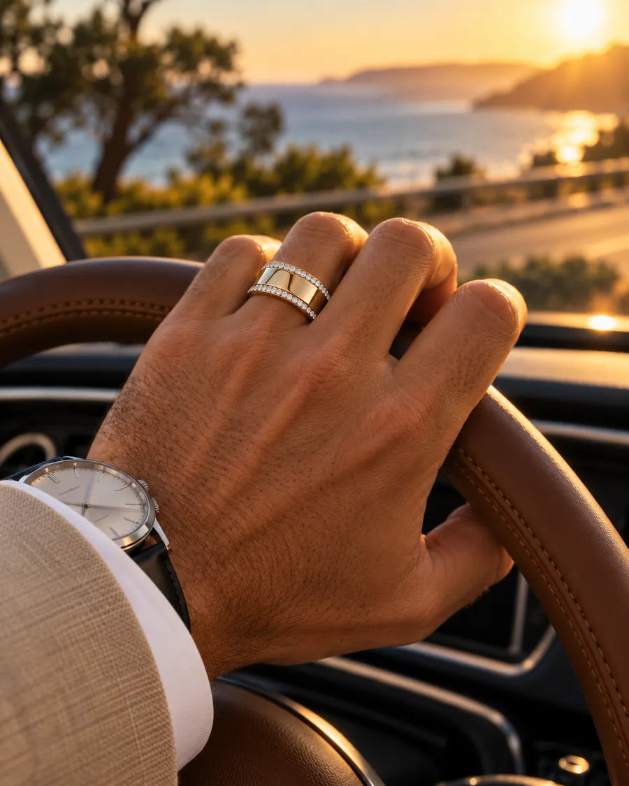 Man wearing HALO Round in 14k white gold over a gold Oura Ring, hand on the steering wheel on a coastal drive at sunset